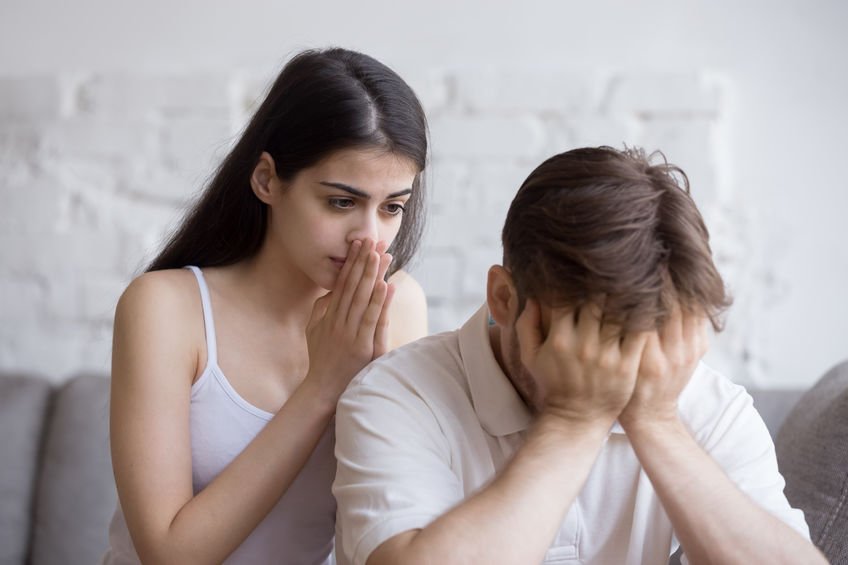 young lady worries about her partner as he clasps his head in his hands