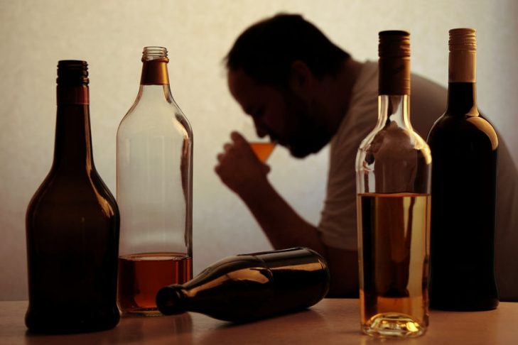 male drinking alcohol whilst surrounded by used bottles