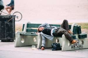 man laying with eyes closed on a public bench