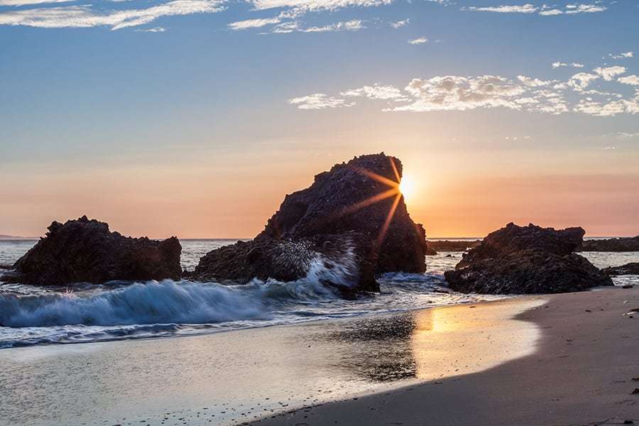 waves hitting the rock on the beach at sunset