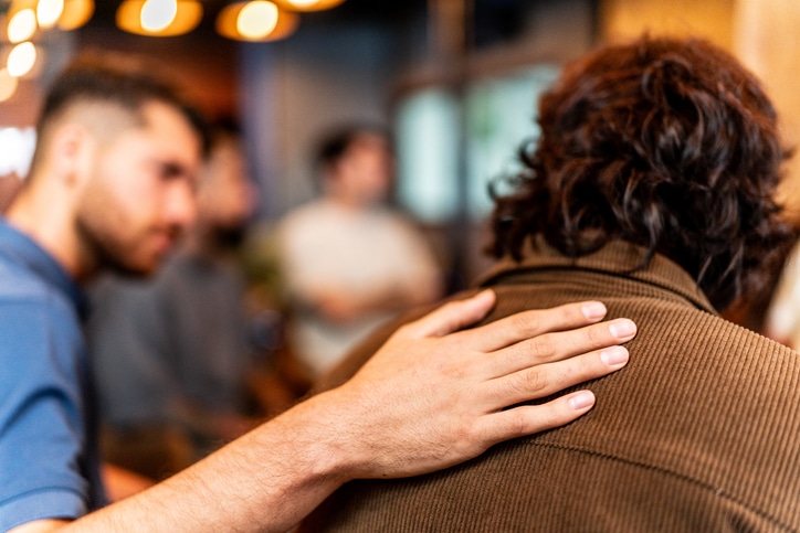 Close-up of man's hand on patient shoulder on a males group xanax addiction treatment therapy at Cornerstone