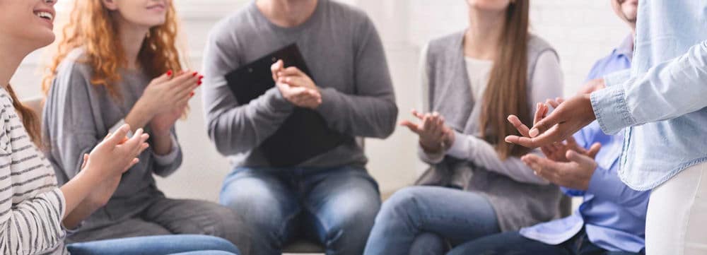 Group of people clap after speaking in group therapy for addiction.