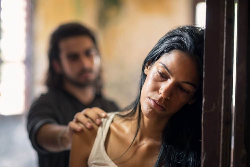 Man reaching out to sad woman leaning on door.